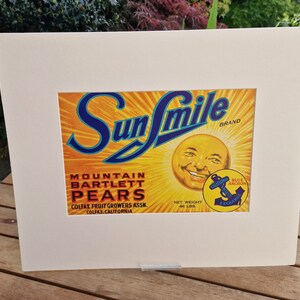 May include: A vintage Sun Smile brand label for Mountain Bartlett Pears. The label features a smiling sun face with a blue anchor logo and the text "Blue Anchor California Fruit Exchange".