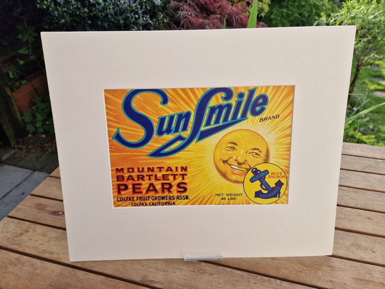 May include: A vintage Sun Smile brand label for Mountain Bartlett Pears. The label features a smiling sun face with a blue anchor logo and the text "Blue Anchor California Fruit Exchange".
