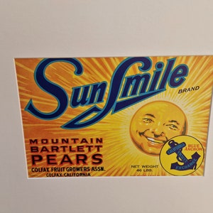 May include: A vintage label for Sun Smile brand Mountain Bartlett Pears. The label features a smiling sun with a blue anchor logo and the text "California Fruit Exchange". The label is yellow, orange, and blue.