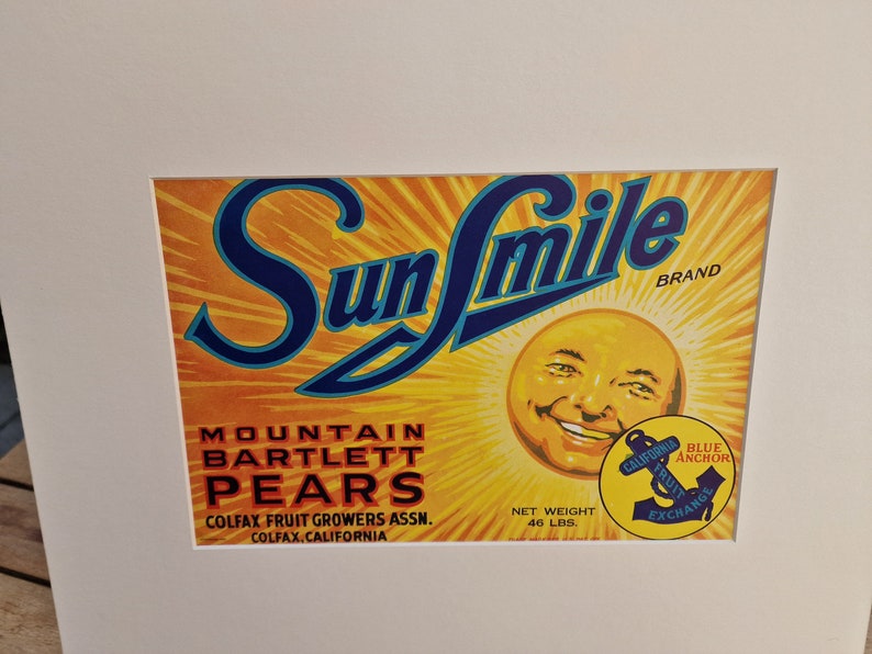 May include: A vintage label for Sun Smile brand Mountain Bartlett Pears. The label features a smiling sun with a blue anchor logo and the text "California Fruit Exchange". The label is yellow, orange, and blue.