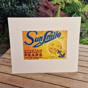 May include: Vintage Sunsmile Brand Mountain Bartlett Pears label featuring a smiling sun face and a blue anchor logo. The label is yellow, orange, and blue with white text. The text reads "Sunsmile Brand", "Mountain Bartlett Pears", "Colfax Fruit Growers Assn.", "Colfax, California", and "Net Weight 48 Lbs".
