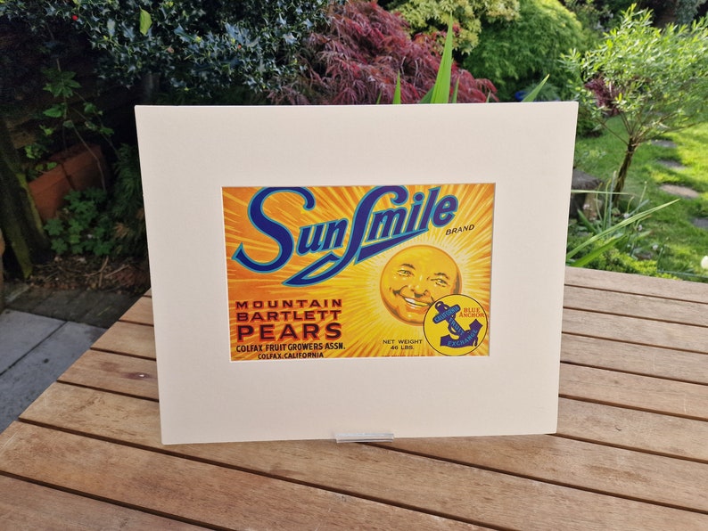 May include: Vintage Sunsmile Brand Mountain Bartlett Pears label featuring a smiling sun face and a blue anchor logo. The label is yellow, orange, and blue with white text. The text reads "Sunsmile Brand", "Mountain Bartlett Pears", "Colfax Fruit Growers Assn.", "Colfax, California", and "Net Weight 48 Lbs".