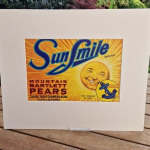 May include: Vintage Sun Smile brand label for Mountain Bartlett Pears. The label features a smiling sun face with a blue anchor logo and text that reads "California Fruit Exchange". The label is yellow, blue, and red with a white background.