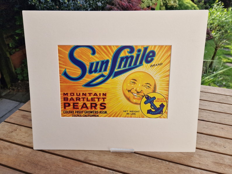 May include: Vintage Sun Smile brand label for Mountain Bartlett Pears. The label features a smiling sun face with a blue anchor logo and text that reads "California Fruit Exchange". The label is yellow, blue, and red with a white background.