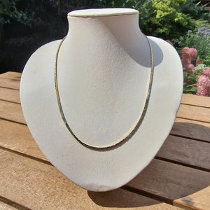 Puede incluir: Un collar de cadena de oro en un busto de maniquí blanco. El collar es un diseño simple y delicado.