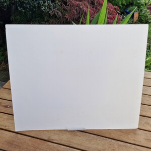 May include: A white, rectangular, acrylic sheet with a silver metal stand. The sheet is sitting on a wooden surface.