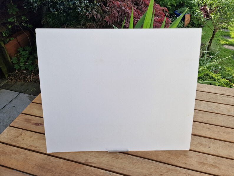 May include: A white, rectangular, acrylic sheet with a silver metal stand. The sheet is sitting on a wooden surface.