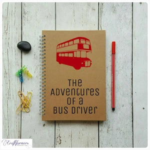 Peut inclure: Un carnet brun avec une reliure spirale. La couverture présente un bus à impériale rouge et le texte "THE ADVENTURES OF A BUS DRIVER".