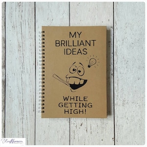 May include: A brown spiral notebook with the text "My Brilliant Ideas While Getting High!" and a cartoon face with a lightbulb above it.