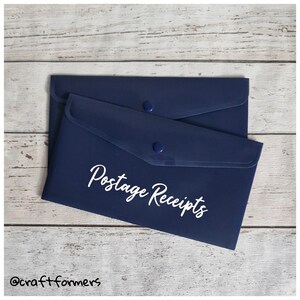 May include: Two navy blue document holders with snap closures. The top holder has the words "Postage Receipts" in white script. The holders are on a light wood grain surface.