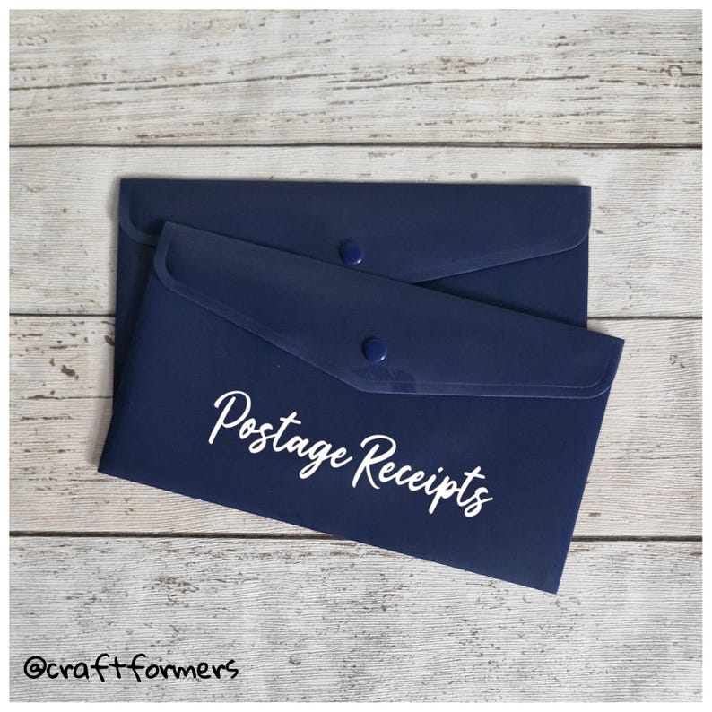 May include: Two navy blue document holders with snap closures. The top holder has the words "Postage Receipts" in white script. The holders are on a light wood grain surface.