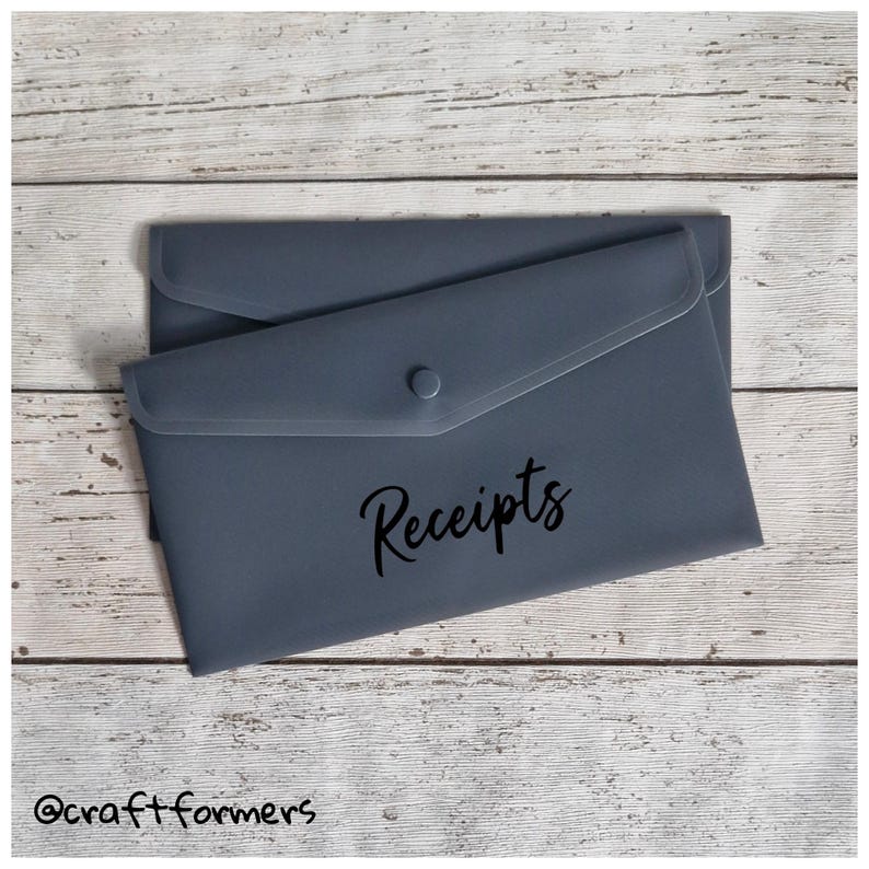 May include: A slate blue receipt holder with a button closure. The word "Receipts" is written in a cursive font on the front of the holder. The holder is on a light wood grain surface.