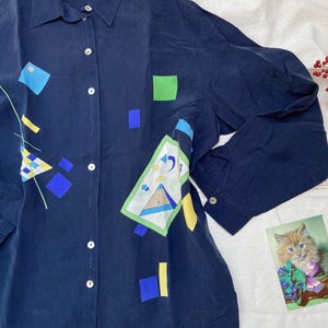 May include: A navy blue long-sleeved button-up shirt with a geometric pattern in shades of blue, green, yellow, and white. The shirt has a collar and a button-up front.