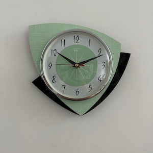 May include: A green and black wall clock with a silver face and black hands. The clock has a unique design with two black triangles on either side of the clock face.