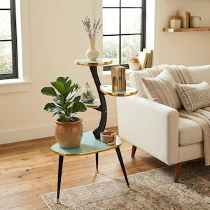 Op de afbeelding: Een plantenstandaard met meerdere niveaus met een zwart gebogen frame en drie ronde, turquoise planken met gouden rand. Het bevat een potplant, een vaas met gedroogde bloemen en decoratieve items. De poten zijn zwart met gouden uiteinden.