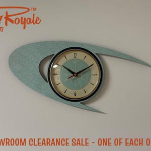 May include: A wall clock featuring a light blue, asymmetrical, wing-shaped frame with a circular face. The clock face has a cream-coloured background, a light blue centre, black numerals, and black hour and minute hands with a red second hand.