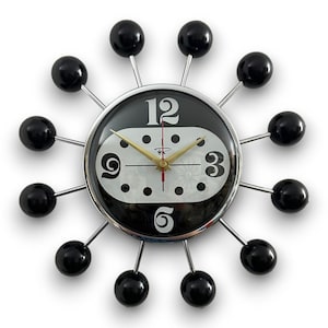 May include: A black and white clock with a silver frame and black ball accents. The clock face has a white background with black numbers and a gold hour hand and red minute hand.