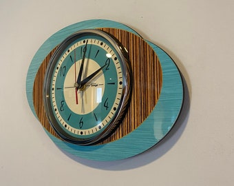 May include: A teal and brown oval clock with black hands and a white face. The clock has a silver rim and black numbers.