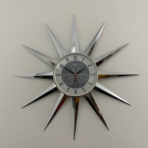 May include: A silver starburst clock with black numbers and a gray face. The clock has a red second hand and a silver frame.