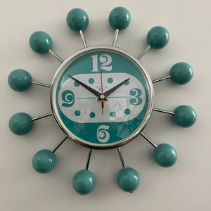 May include: A teal blue clock with white numbers and a silver frame. The clock has 12 round teal blue knobs that are attached to the frame.