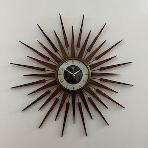 Peut inclure: Une horloge en bois brun avec un design en forme de soleil et un cadran blanc. L'horloge a des chiffres romains noirs et des aiguilles noires. L'horloge a un diamètre de 76 cm.