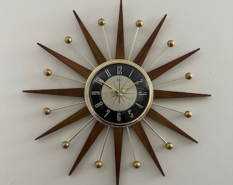 May include: A mid-century modern wall clock with a black face and gold accents. The clock has a starburst design with wooden rays and gold-toned metal balls at the ends of each ray.