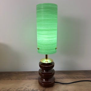 May include: A green glass lampshade with a brown ceramic base. The lampshade has a striped pattern and the base has a layered design.