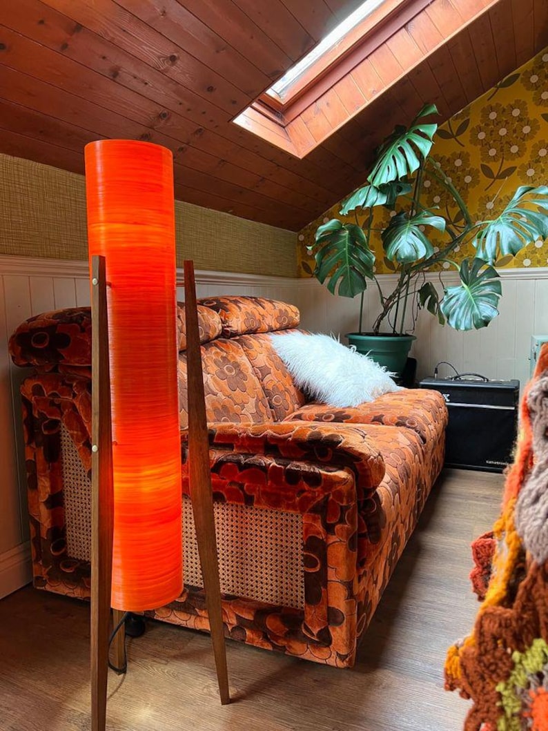 May include: A mid-century modern living room with a bright orange floor lamp, a patterned orange couch, and a large green plant in a terracotta pot.