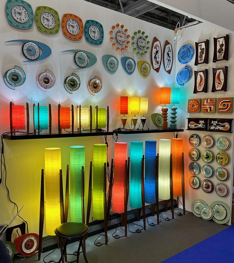 May include: A wall display of colorful mid-century modern lamps and clocks. The lamps are made of woven bamboo and come in a variety of colors, including yellow, green, blue, and red. The clocks are all round and have a variety of designs, including abstract patterns and geometric shapes.