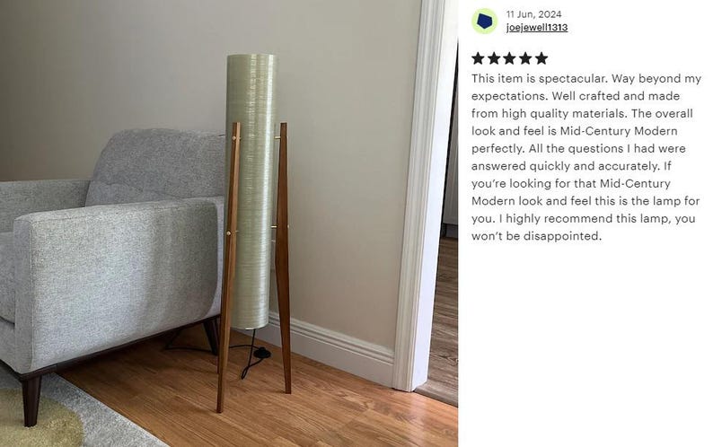 May include: A tall, cylindrical floor lamp with a white, textured shade and a wooden tripod base. The lamp is standing on a wooden floor next to a gray armchair.
