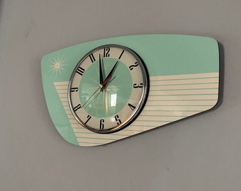 Könnte beinhalten: Eine türkisfarbene und weiße Wanduhr im Mid-Century-Modern-Stil mit silbernem Rand und schwarzen Zahlen. Die Uhr hat eine einzigartige, leicht abgewinkelte Form.