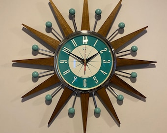 May include: A teal and white clock with a starburst design. The clock has a silver frame and black hands. The starburst design is made of wood and has teal accents.