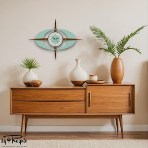 May include: A mid-century modern wall clock with a turquoise and brown design. The clock has a starburst shape with an oval center and a light blue face. The clock is mounted above a wooden cabinet with two drawers and a door.