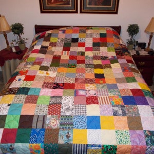 May include: A colorful patchwork quilt with a variety of fabrics and patterns. The quilt is made up of squares of different colors and designs, and it is quilted with a white thread. The quilt is on a bed with two nightstands and lamps.