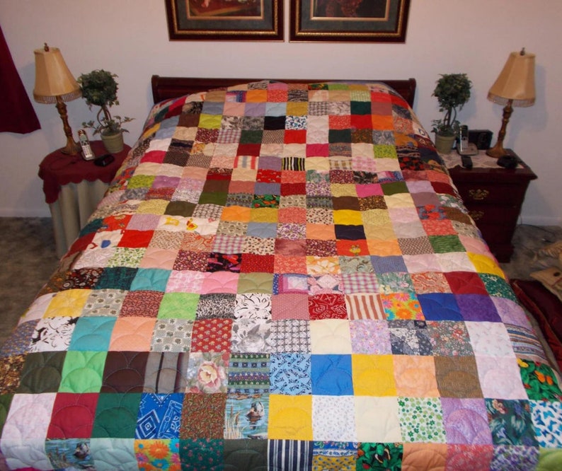 May include: A colorful patchwork quilt with a variety of fabrics and patterns. The quilt is made up of squares of different colors and designs, and it is quilted with a white thread. The quilt is on a bed with two nightstands and lamps.