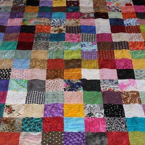 May include: A colorful patchwork quilt with a variety of fabrics and patterns. The quilt is made up of squares of different colors and designs, including floral prints, geometric patterns, and solid colors. The quilt is stitched together with a wavy quilting pattern.