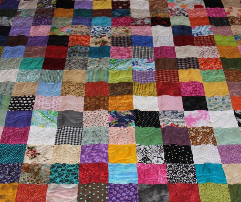 May include: A colorful patchwork quilt with a variety of fabrics and patterns. The quilt is made up of squares of different colors and designs, including floral prints, geometric patterns, and solid colors. The quilt is stitched together with a wavy quilting pattern.