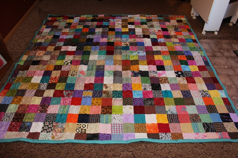 May include: A large patchwork quilt with a teal border. The quilt is made up of hundreds of small squares of fabric in various colors and patterns.
