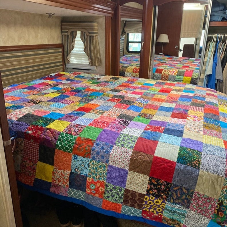 May include: A colorful patchwork quilt with a variety of floral and geometric patterns in shades of red, blue, green, yellow, and purple. The quilt is made of squares sewn together to create a large, rectangular design.