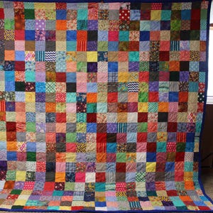 May include: A large patchwork quilt with a blue border. The quilt is made up of hundreds of small squares of fabric in various colors and patterns.