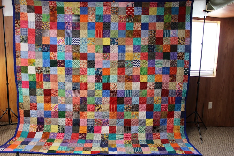 May include: A large patchwork quilt with a blue border. The quilt is made up of hundreds of small squares of fabric in various colors and patterns.