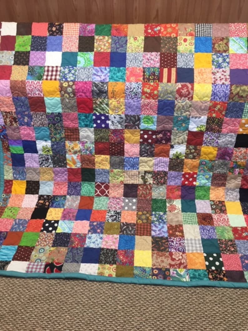 Pode incluir: Uma colcha de retalhos colorida feita de muitos quadrados de tecido diferentes. A colcha &eacute; feita em uma variedade de cores, incluindo vermelho, azul, verde, amarelo e roxo. A colcha &eacute; acolchoada com um padr&atilde;o simples de pequenos c&iacute;rculos.