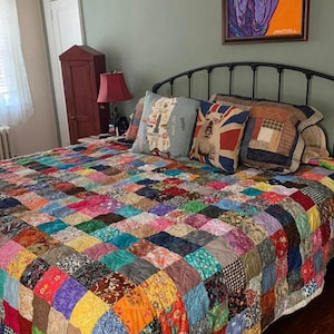 May include: A bed with a colorful patchwork quilt, featuring a variety of fabrics and patterns. The bed has a black metal headboard and is made up with several pillows, including one with a Union Jack design.