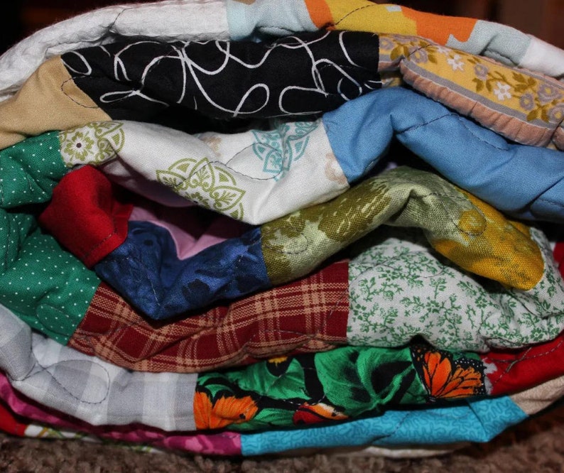 May include: A colorful patchwork quilt with various patterns and fabrics, including polka dots, floral prints, and plaid. The quilt is folded and stacked, showcasing the different layers and textures.