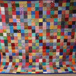 May include: A large quilt made of many colorful fabric squares, each with a different pattern. The quilt is bordered with a dark blue fabric.