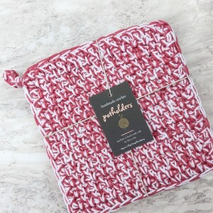 May include: Handmade crochet pot holders in pink and white. The pot holders are tied together with twine and have a tag that says "handmade crochet pot holders" and instructions for machine or hand wash cold, lay flat to dry.
