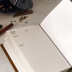 May include: A brown leather-bound recipe journal with lined pages. The journal is open to a page with the heading "Recipe:" and sections for "Prep Time:", "Ingredients:", and "Method:".