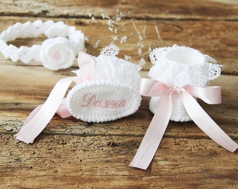 Könnte beinhalten: Weiße gehäkelte Babyschuhe mit rosa Satinbändern und Spitzenbesatz. Ein Schühchen ist mit dem Namen "Dasha" bestickt.