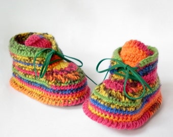 May include: A pair of colorful, crocheted baby booties. The booties are made with a variety of yarn colors, including pink, orange, yellow, green, and blue. Green elastic laces are tied in a bow. The booties are designed to keep a baby's feet warm.