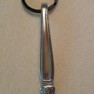 May include: A silver spoon keychain with a decorative handle and a black metal key ring.